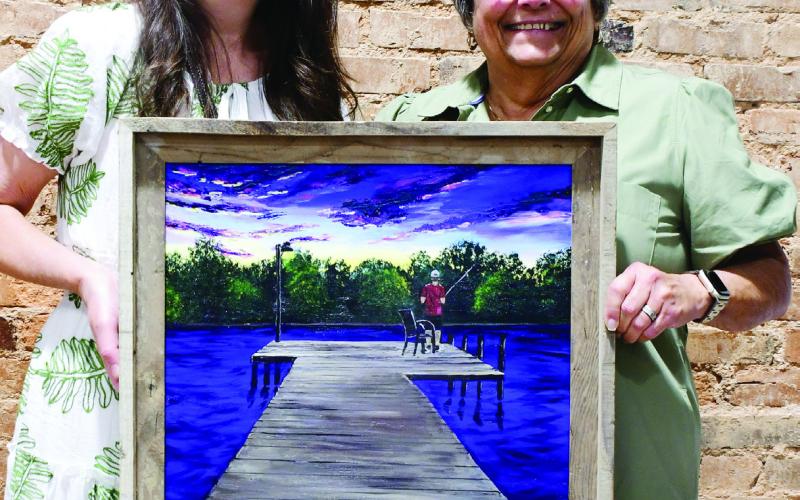 Artist Krista Kugaraj (left) displays her painting of a Lake Sinclair dock, inspired by a story written by GWM board member Gloria Edge.