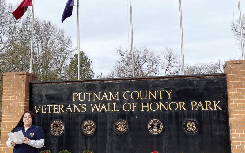 Local VFW Commander Nikki Barker speaks at Putnam County Veterans Wall of Honor Park. Behind her are ceremonial wreaths, all with the American flag along with the different branches of armed forces: Army, Marine Corps, Air Force, Navy, Coast Guard, and Space Force. EMME CLAUSE/Staff