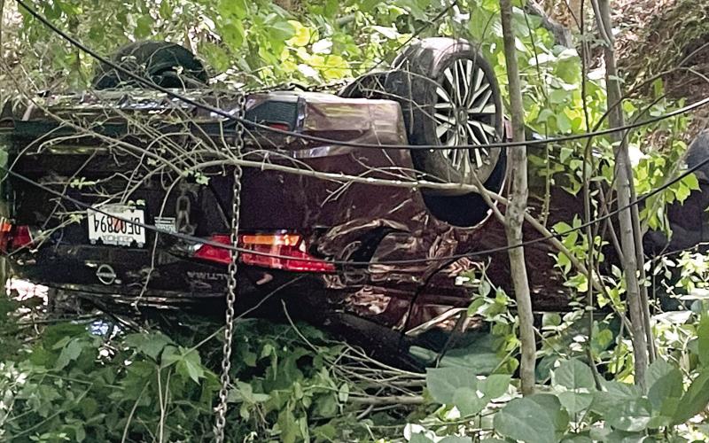 A chain hangs from the overturned Nissan as Hurt’s Towing prepares to remove it from the woods at the end of East Sumter Street Monday. LYNN HOBBS/Staff