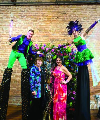 Sara Tomson-Hooper and Myrna Taylor pose under the floral frame with performers from Gravity Entertainment.