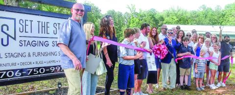 Sean and Sara Tintle (center, behind bow) with Eatonton-Putnam Chamber of Commerce CEO Robbie King (sunglasses) celebrate the official ribbon cutting for Set the Stage, their new business venture off Scott Road in eastern Putnam County.