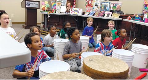 First and second graders perform the rhythm to the Mario theme as the board watches from behind in their seats.