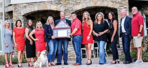 Members of the Kim and Lin Logan Team display a flag once flown over Camp Arifjan in Kuwait, presented to them by U.S. Army National Guard Major Brett Thomas in recognition of their support of “citizen soldiers” abroad.
