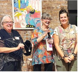 L-R: Art show chairperson Michele Hartung and co-chair Cathy McIntire congratulate The Artisans Village communications specialist Melanie Schneider after she won a Merit Award for “Golden Spiral,” a necklace she designed and created. IAN TOCHER/Staff