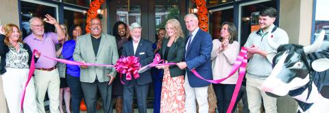 Eatonton-Putnam Chamber of Commerce President Robbie King (center with bow) watches as Courtney Adkinson cuts the ribbon with her husband Frank at her side, to officially announce the opening of Luxury Outdoor Travel, near Publix in Greene County. IAN TOCHER/Staff
