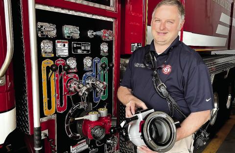 Eatonton Fire Department Chief Jamey Williamson holds one of the new 5-inch hose fittings he’s already received to replace the current 3-inch fittings (red fixture by his right hip). Now, he’s just awaiting delivery of new 5-inch fire hoses to install everything on the department’s trucks. IAN TOCHER/Staff
