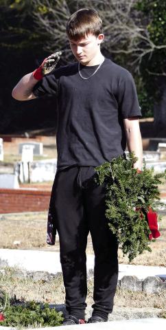 A young man, accompanied by his family nearby, salutes a veteran’s grave at Pine Grove Cemetery after placing a wreath as part of the Wreaths Across America program. IAN TOCHER/Staff