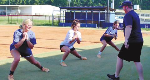From left, Senior Jada McDerment Senior Sara Hulsey and Junior `Lily Frisch are led in a pitching exercise by Coach McElroy during summer workouts last week.