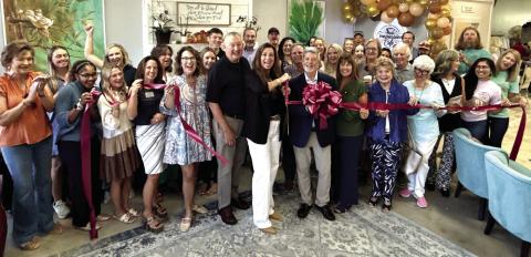 With husband Steve at her back, Compassion Café owner Lisa Tubbs wields the scissors for a ribbon-cutting ceremony arranged by Robbie King (behind bow) of the Eatonton-Putnam Chamber of Commerce. IAN TOCHER/Staff