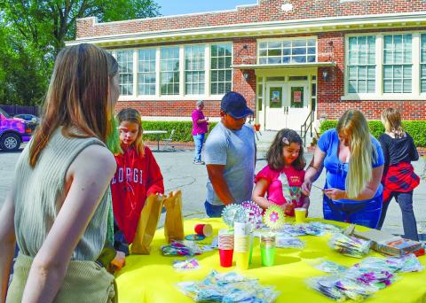 Katie Lopez helps her daughter Melanie Lopez to make a flower in a cup as Gerardo Lopez looks on, volunteer Madison Martin unravels a string, and volunteer Amy Moss watches the process.