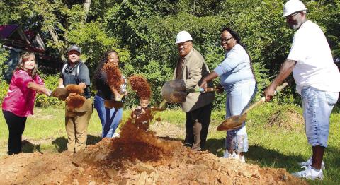 With tiny Journiee Burnney peering out from the center, her mother Ikeirra beside her was joined by (l-r) Habitat board member Linda Moore, builder Clark Harper, Eatonton Mayor John Reid and other family members as they each tossed a ceremonial shovelful of dirt for the World Habitat Day groundbreaking.