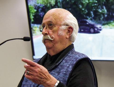 With a video of the intersection of Twin Bridges and Dennis Station Roads playing on screens behind him, past county chairman Billy Webster addressed the current Putnam County Commission about the intersection’s safety issues. IAN TOCHER/Staff
