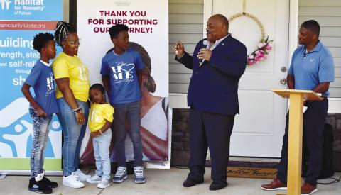Eatonton Mayor John Reid hands over the keys to a brand-new Habitat home to Cerria and her three kids while former NFL star Warrick Dunn enjoys the moment.