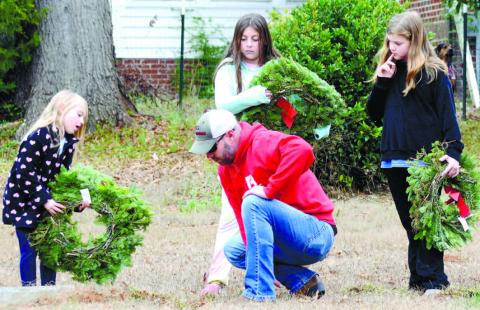 Jason Riddle clears dirt and grass from a veteran’s marker at Eatonton’s Pine Grove Cemetery, as daughters Tiffany and Teagan watch, along with their cousin Rachel Paul (right). IAN TOCHER/Staff