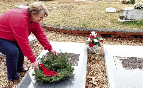 A Wreaths Across America volunteer lays a wreath on a veteran’s grave at Pine Grove Cemetery while solemnly thanking them for their service. EMME CLAUSE/Staff