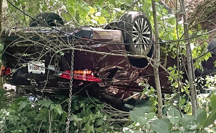 A chain hangs from the overturned Nissan as Hurt’s Towing prepares to remove it from the woods at the end of East Sumter Street Monday. LYNN HOBBS/Staff